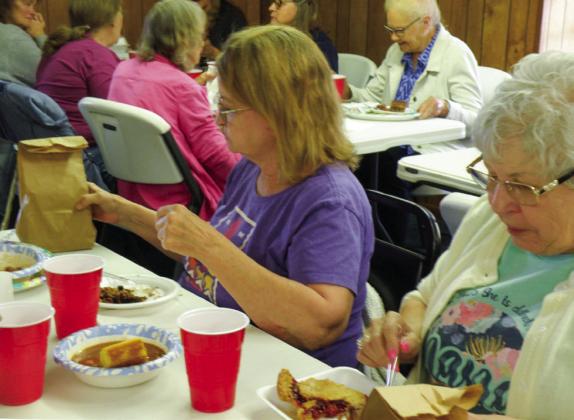 Following the Easter Luncheon, Becky Hightower, left, and Gail Trammel enjoy dessert, which included homemade cherry pie. The brown bags, left by the Easter Bunny, were filled with take-home treats, including cookies and candies.