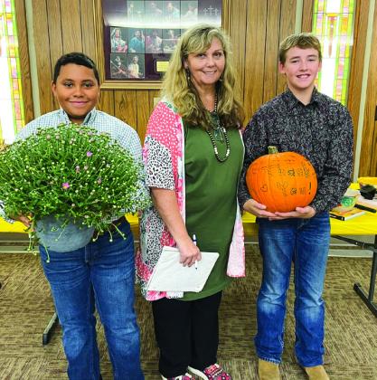 Bryson Session, left, and Slade Chapman, right, present Sandy Koepke with a “thank you” pumpkin and mum for all her hard work and volunteering during the Childress County 4-H Food and Nutrition Project.