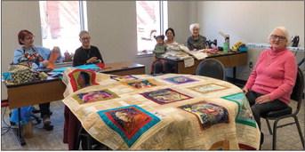 Collingsworth County quilters, including GiGi Waller, left, Pat Barnett, Catalina and Roxanne Smith, Linda Powell and Judy Cudd, set up sewing machines in the north meeting room of Wellington Senior Citizens Center on Wednesday, Feb. 15. Cudd sits in awe of the detailed quilt displayed in the center and crafted by Katy Taylor, not pictured, as well as Lennie Statham and Margret Wood. The Red River Sun/Bev Odom
