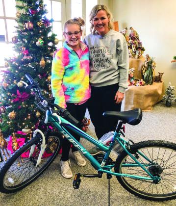 Wellington Elementary fifth-grader Ava Kate Inman, along with her mother, Amy Inman, accept the bicycle she won in a drawing during the December Lighting of the Square. Collingsworth Chamber of Commerce President Karen Caldwell made the presentations in the Collingsworth County Museum Ellis Art Center.