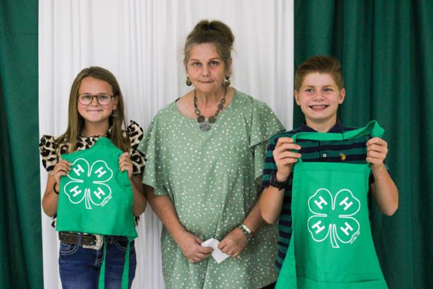 Childress County 4-H Foodies Cambri Willis, left, and David Rister, right, receive their Clover aprons from Childress County 4-H Volunteer Sandy Koepke.