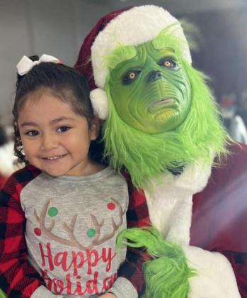 Four-year-old Evelyn Sanchez makes a new friend in The Grinch during the Collingsworth County Home Delivered Meals breakfast fundraiser event.