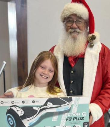 WellingtonElementarySchool third-grader Piper Barnes collects the hoverboard prize from Santa during the fundraiser drawing. Everyone in attendance entered their name on the back of their ticket for a chance to win a hoverboard.