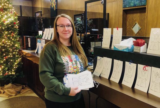 In between waiting on customers at the holiday event, Trinity Sanderson displays the Child Protective Services (CPS) Angels across the counter available for adoption by bank patrons. Once an angel is selected, the item listed on the front needs to be wrapped and returned to the bank by 3 p.m. Monday, Dec. 16.