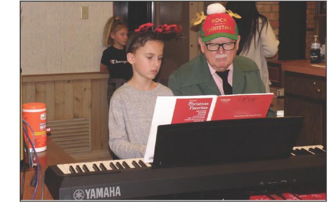 Monson Music Studio students, including Carter Keys, left, and Skylar Williams, back, performed Christmas carols, accompanied by music instructor Gerald Monson, right, at the Peoples Federal Credit Christmas Open House.