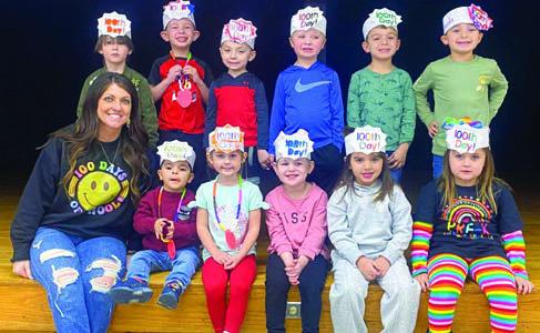 Wellington Elementary School teacher Megan Wischkaemper and her pre-kindergarten students display their 100th day of school head pieces, which read,“hip, hip, hooray for the 100th day,” on the stage in the elementary cafeteria.