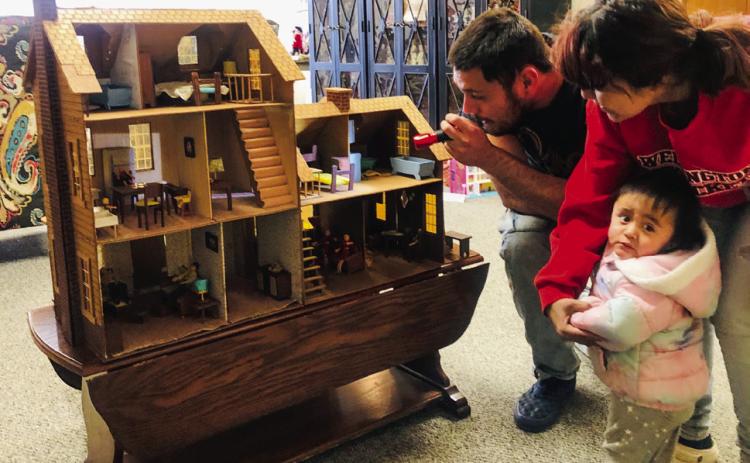 Collingsworth County Museum visitors Enrique Rojas and Stephanie Garcia, along with one-year-old daughter Nevaeh, peer into the dollhouse kit ordered by Phyllis Floyd for her daughters. Purchased from Sears &amp; Roebuck in 1979, her husband, Ray Floyd, had the tedious job of helping assemble the life-like replica. The Red River Sun/Bev Odom