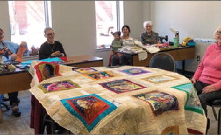 Collingsworth County quilters, including GiGi Waller, left, Pat Barnett, Catalina and Roxanne Smith, Linda Powell and Judy Cudd, set up sewing machines in the north meeting room of Wellington Senior Citizens Center on Wednesday, Feb. 15. Cudd sits in awe of the detailed quilt displayed in the center and crafted by Katy Taylor, not pictured, as well as Lennie Statham and Margret Wood. The Red River Sun/Bev Odom