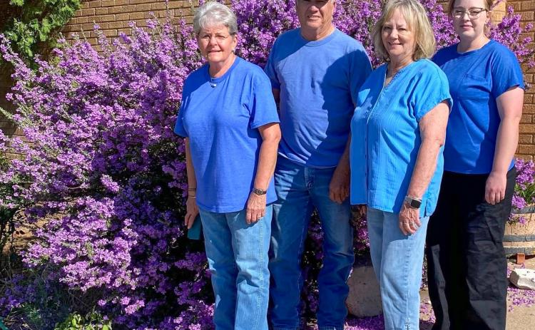 At its best bloom, the SOS from Texas crew admires the vibrant purple blooms of the Texas sage in front of the SOS shop in Samnorwood, headquartered in the former Samnorwood High School. From left: Kathie Lloyd, 15-year employee; owner Gary Oldham; Mona Darrow, 30-year employee; and Allison Bentley, five-year employee. SOS From Texas