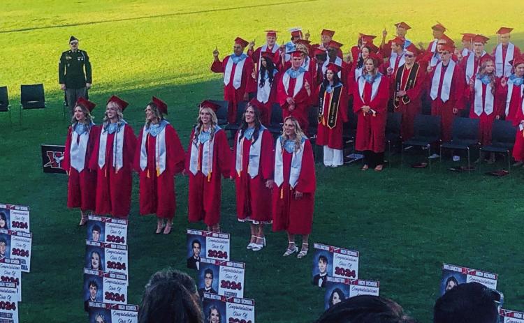 As the evening sun sets behind Skyrocket Football Stadium, Wellington High School Class of 2024 cheerleaders, including Summer Neufeld, left, Kendra Bawcom, Madeleine Kane, Kaitlin Bawcom, Audrey Jones and Presley Kane, lead classmates and the crowd in singing the Alma Mater as the graduation ceremonies for the history-making class come to a close at Powell Field Friday, May 17. The Red River Sun/Bev Odom
